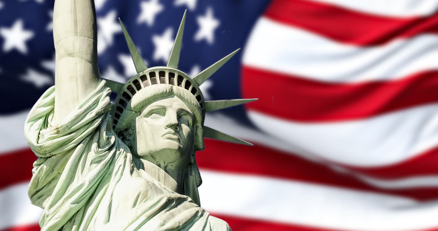 A close-up of the Statue of Liberty's face and crown set against a blurred, waving United States flag, symbolizing the "American Dream" and major US lottery games like Powerball and Mega Millions. American-Lottery-Opportunities